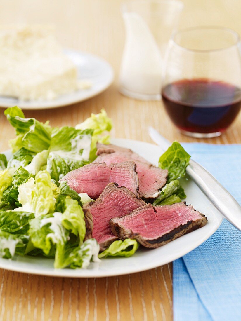 Sliced Beef Over Lettuce with a Creamy Dressing; Glass of Red Wine