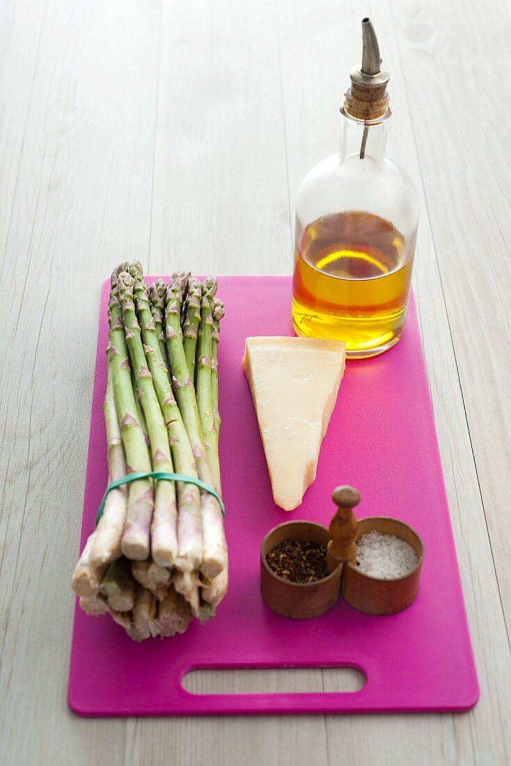 An arrangement of asparagus, cheese, olive oil and spices on a chopping board