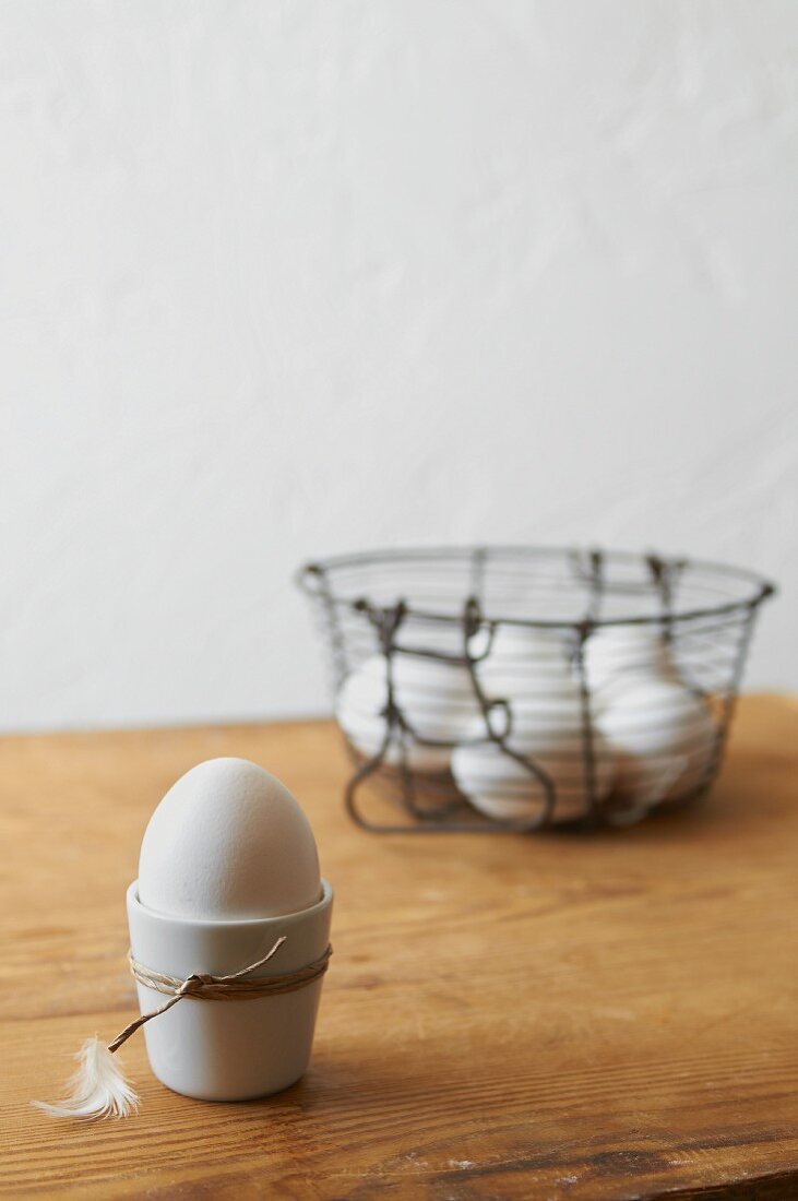 An egg in an egg cup and eggs in a wire basket
