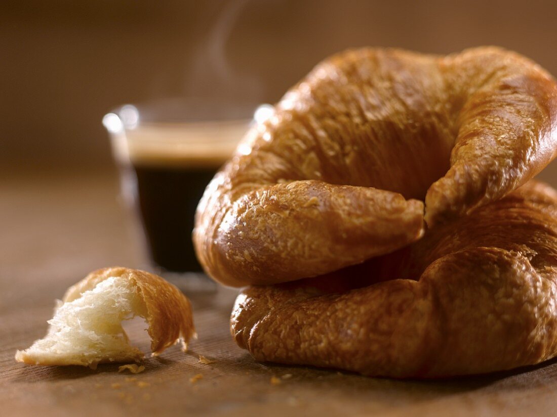Two Croissants Stacked with a Steaming Espresso in the Background