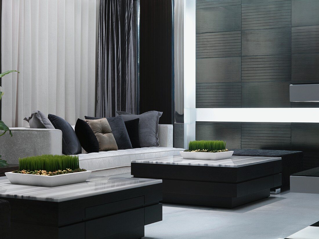 Wohnzimmer in Grau, Schwarz und Weiß mit kompakten, quadratischen Tischen; als grüner Kontrapunkt Schalen mit grünem Gras
