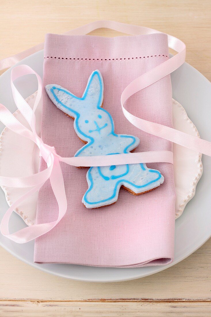 Easter bunny biscuit with pale blue icing on romantic place setting with pink linen napkin
