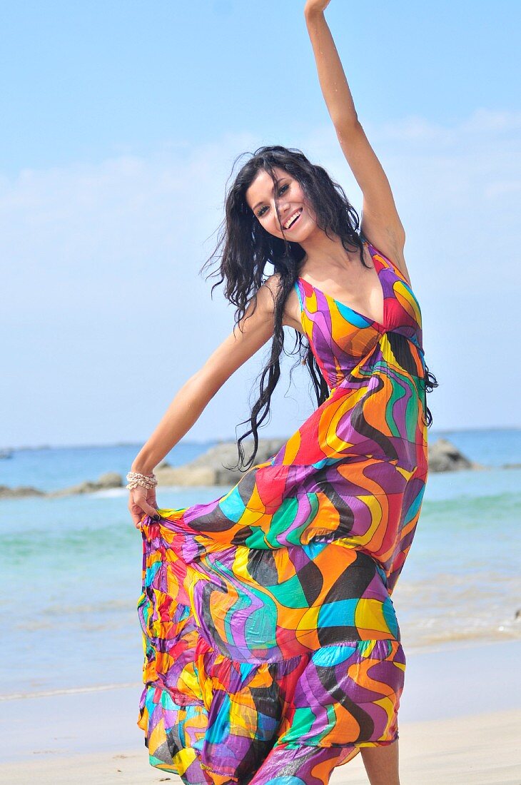 A woman wearing a brightly patterned dress dancing on a beach