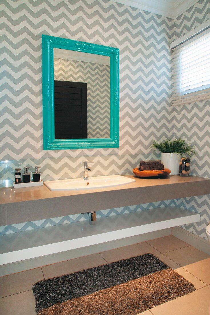 Grey and white, zig-zag wallpaper and mirror with turquoise frame in elegant guest bathroom
