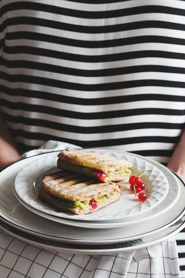 A woman serving a panini with avocado and redcurrants