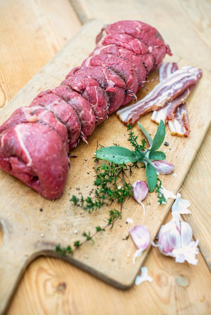 Ready-to-cook beef roulade with ingredients on a wooden chopping board