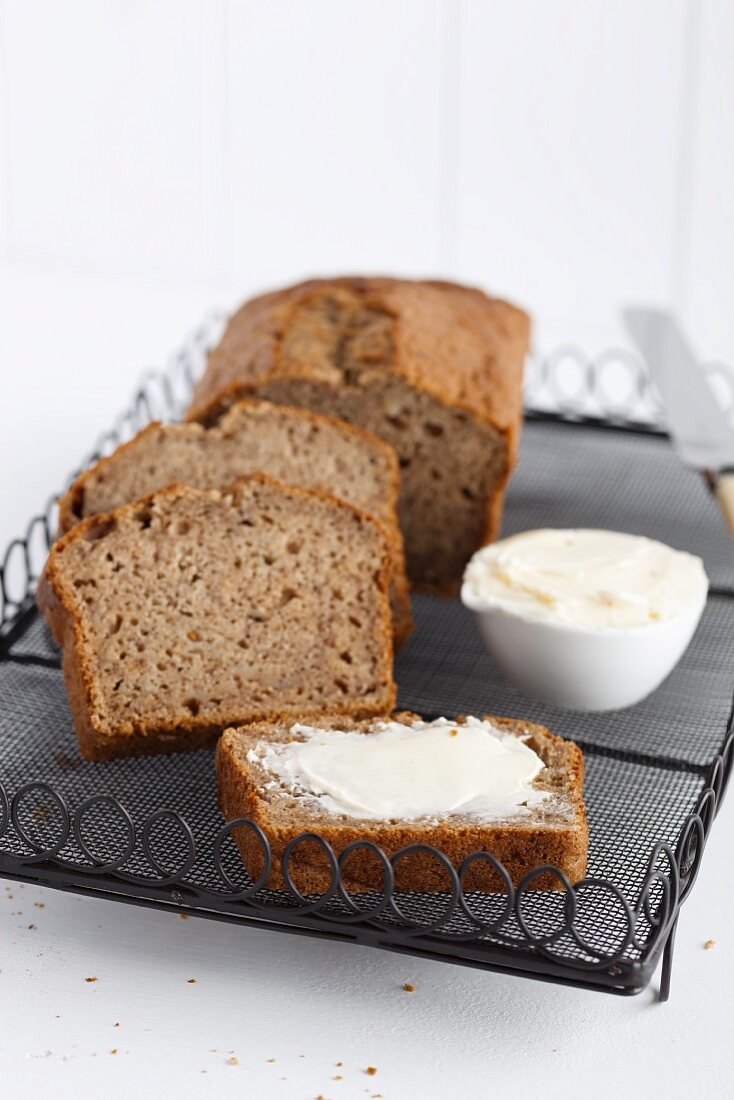 Freshly baked banana bread, sliced, with butter on a cooling rack