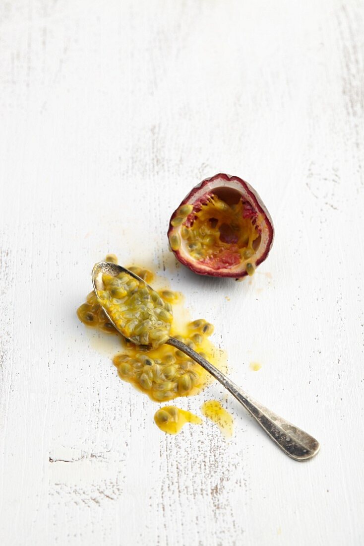A halved passion fruit and a spoon with scooped-out fruit flesh