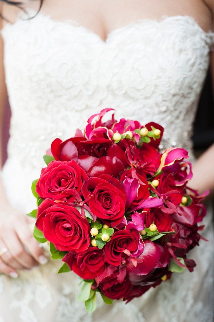A bride wearing a lace dress holding a bouquet of red flowers