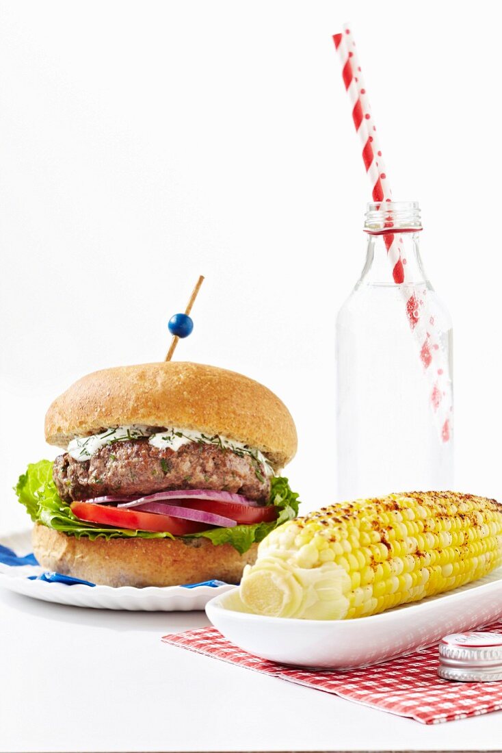A Greek-style hamburger with a spicy corn cob and sparkling water