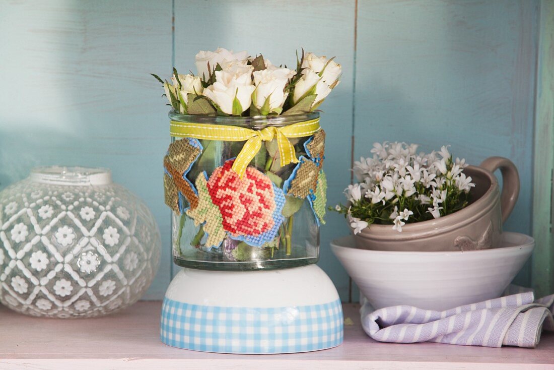 White roses in glass vase decorated with embroidery