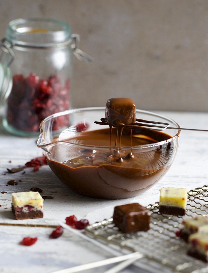A chilli and cranberry praline being lifted out of melted cooking chocolate