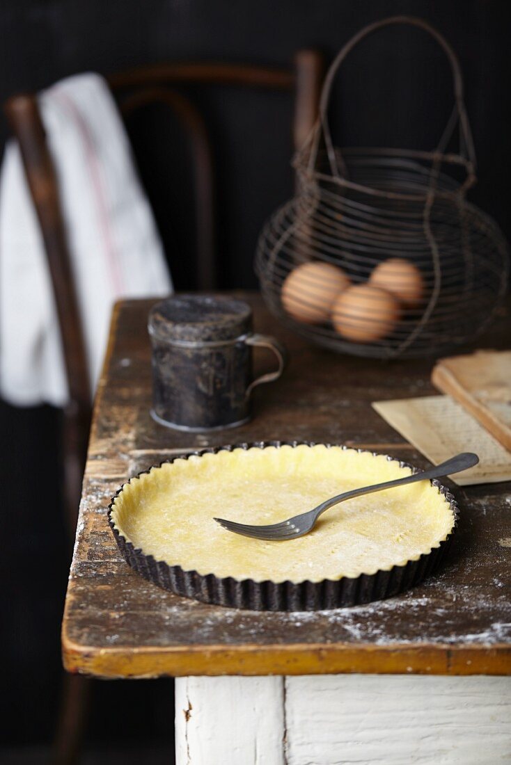 Shortcrust pastry for an apple and frangipane tart being with a fork on a rustic kitchen table
