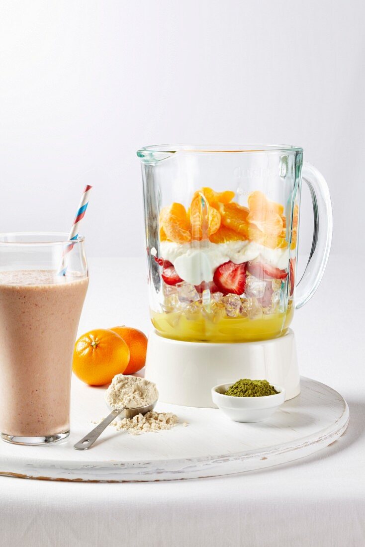 Joghurtshake mit Früchten im Glas und geschichtete Zutaten im Mixer