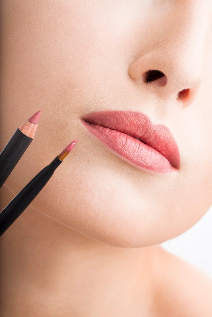 A woman's lips with make-up next to a lip liner and a lip gloss brush
