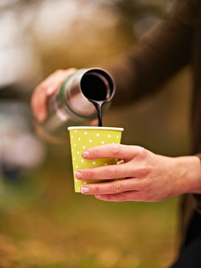 Frau giesst Holunderbeersaft aus Thermosflasche in Becher