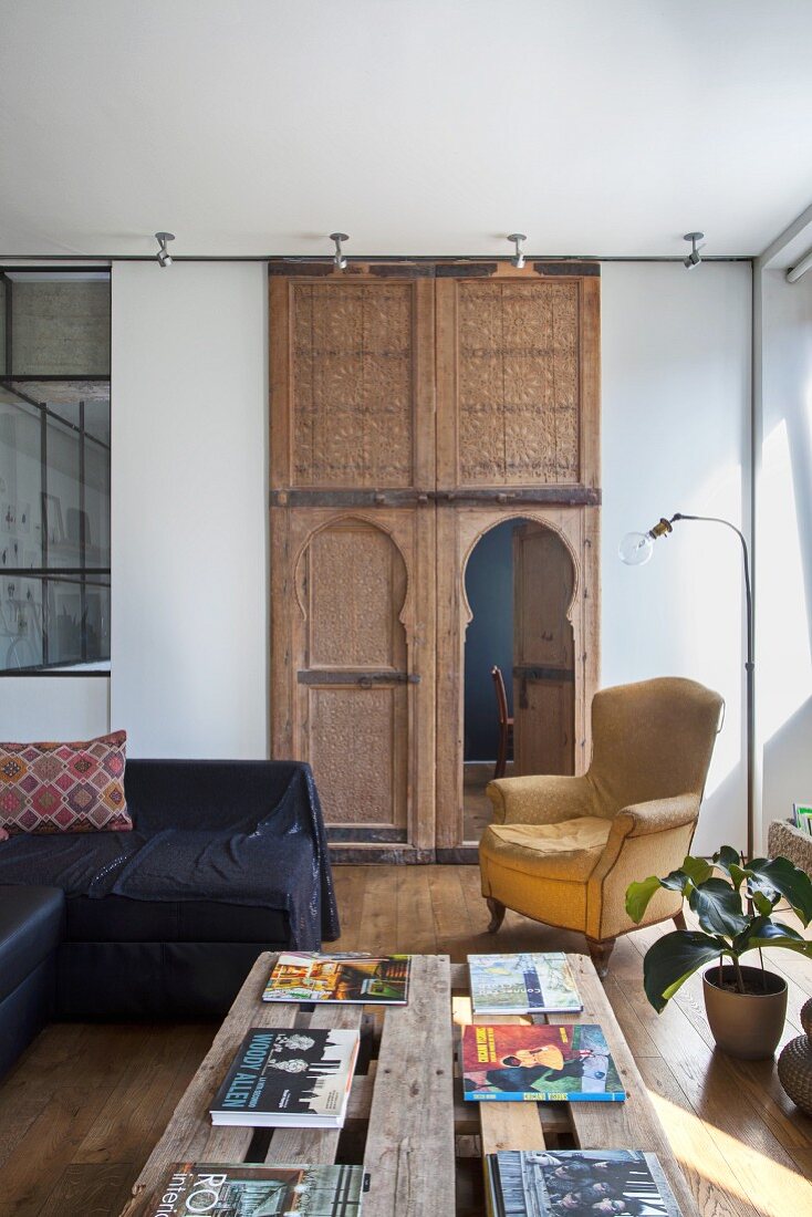 Books on a rustic pallet table and armchair in living area in front of Moroccan ornate wooden elements