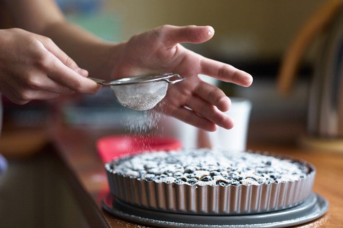 Blueberry tart being dusted with icing sugar