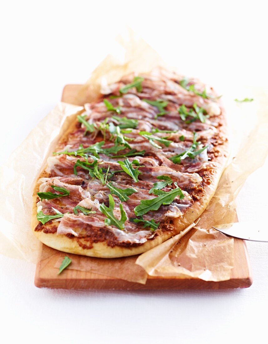 Pizza with pancetta and rocket on a wooden board