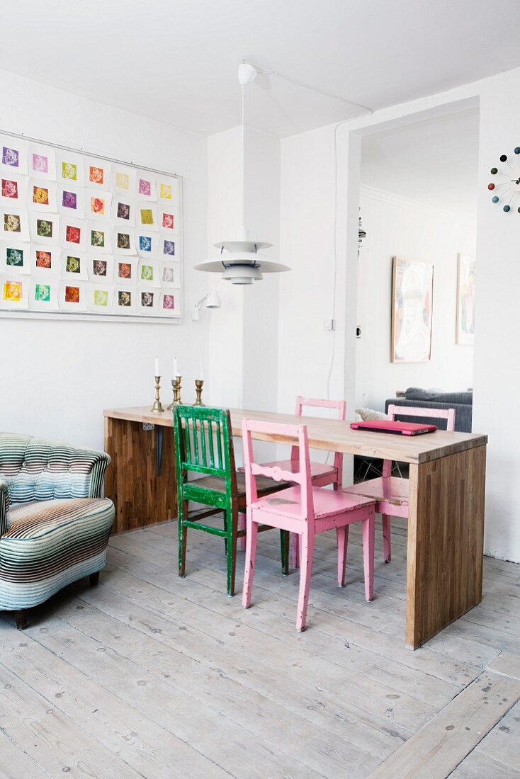 Colourful wooden chairs at minimalist wooden table below classic lamp