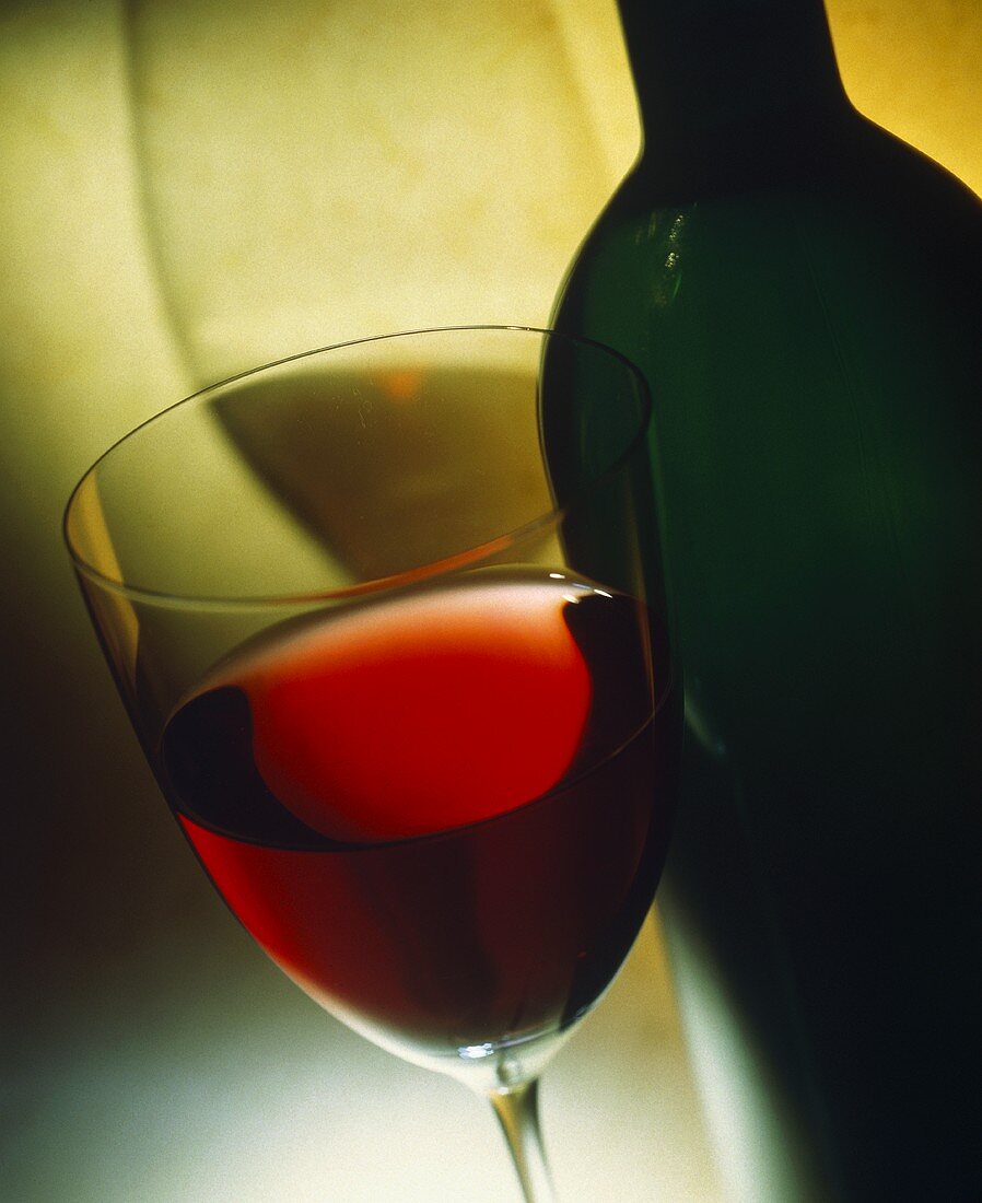 Stillleben mit Rotweinglas vor Flasche ohne Etikett