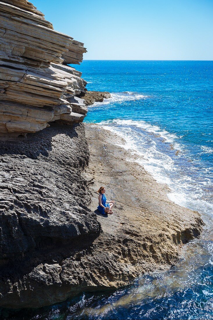 A woman meditating on a cliff by the sea