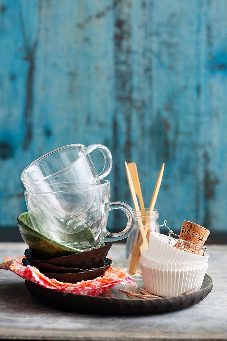 A stack of bowls, glass cups, paper cases and skewers on a tray