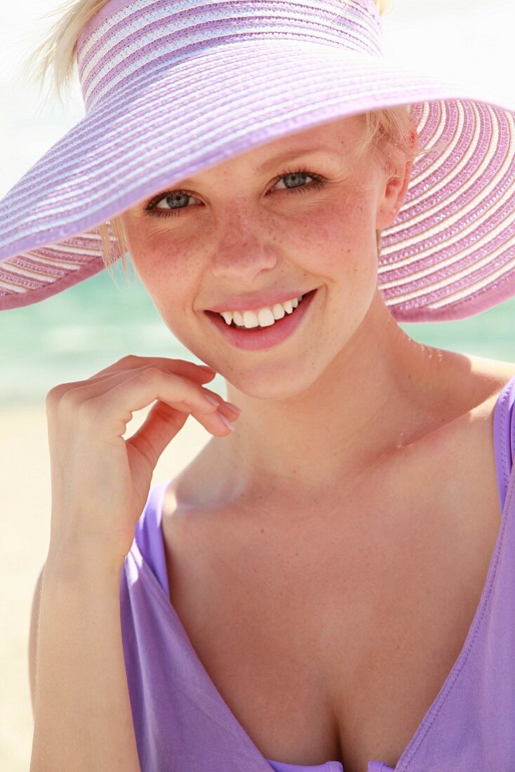 A young woman wearing a purple beach dress and a sun hat