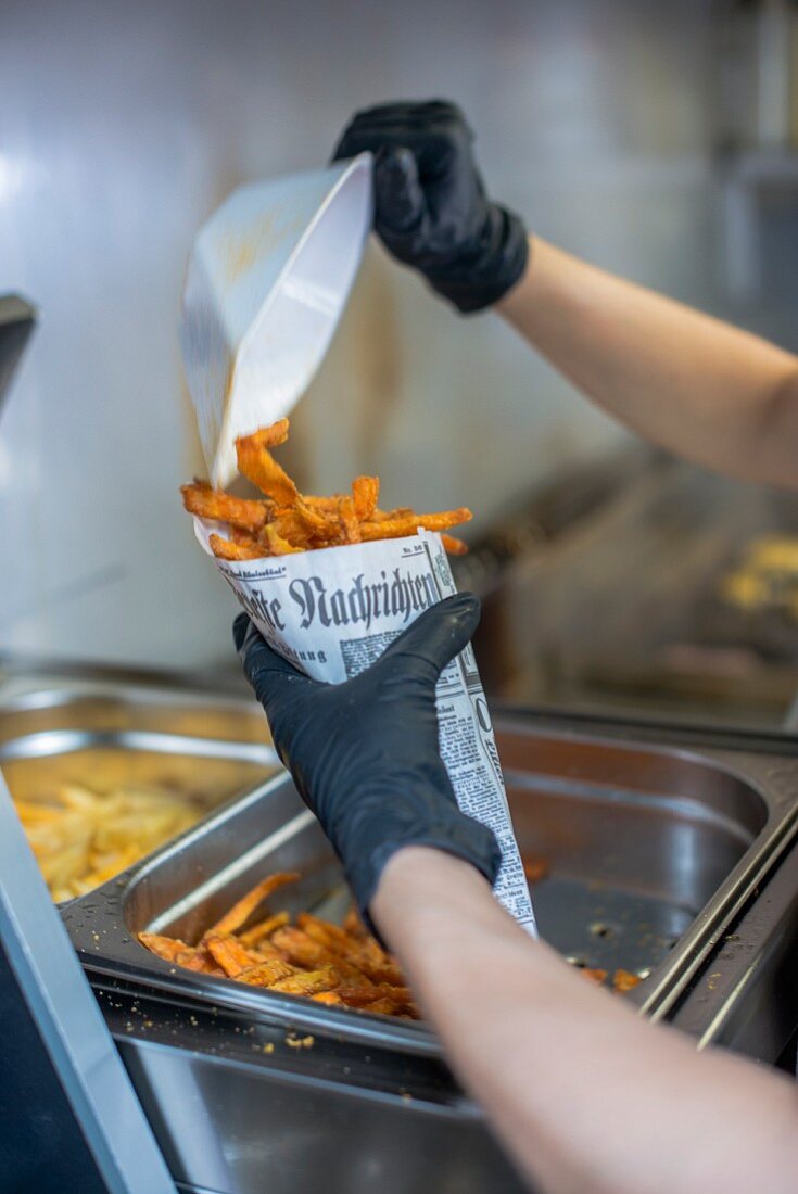 Sweet potato chips being transferred into a newspaper cone