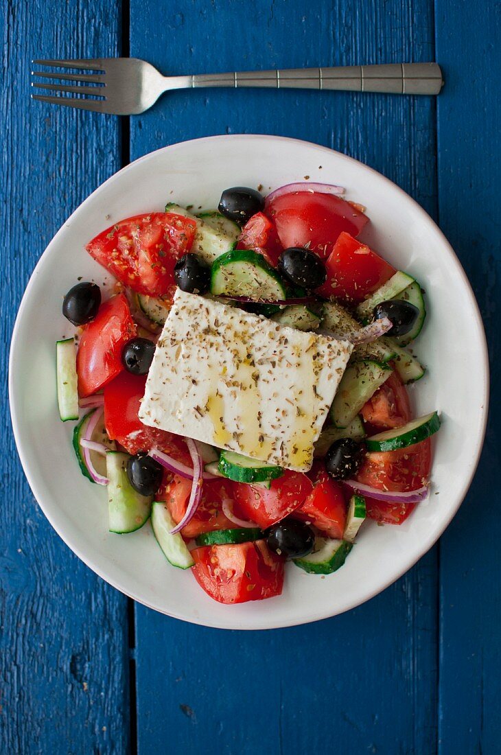 Griechischer Salat mit Tomaten, Gurken, Zwiebeln, schwarzen Oliven, Feta, Olivenöl und getrocknetem Oregano
