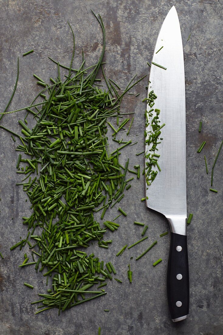 A kitchen knife next to freshly chopped chives