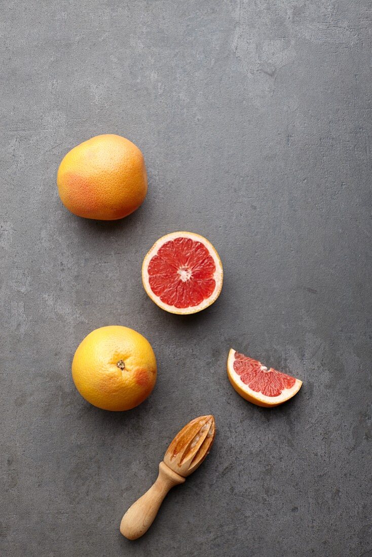 Pink grapefruits, whole and halved, with a wooden juicer (seen from above)