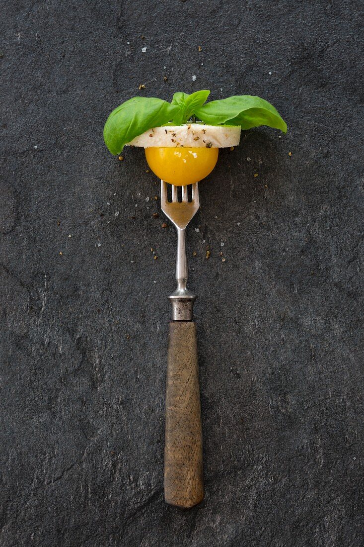 A yellow cherry tomato, a slice of the mozzarella and basil leaves on a fork