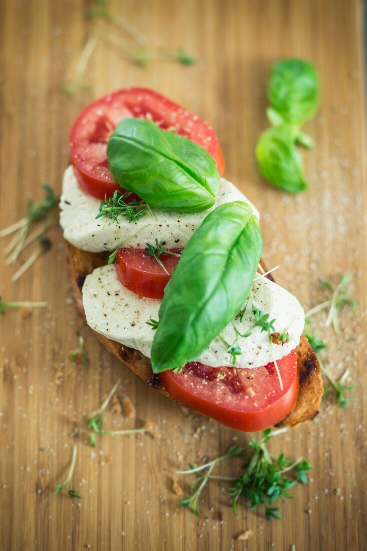A slice of bread topped with tomatoes, vegan mozzarella and basil
