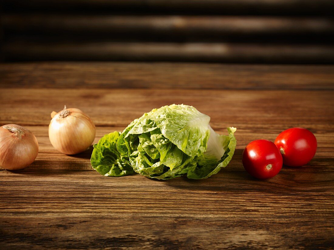 Cos lettuce, tomatoes and onions on a wooden surface