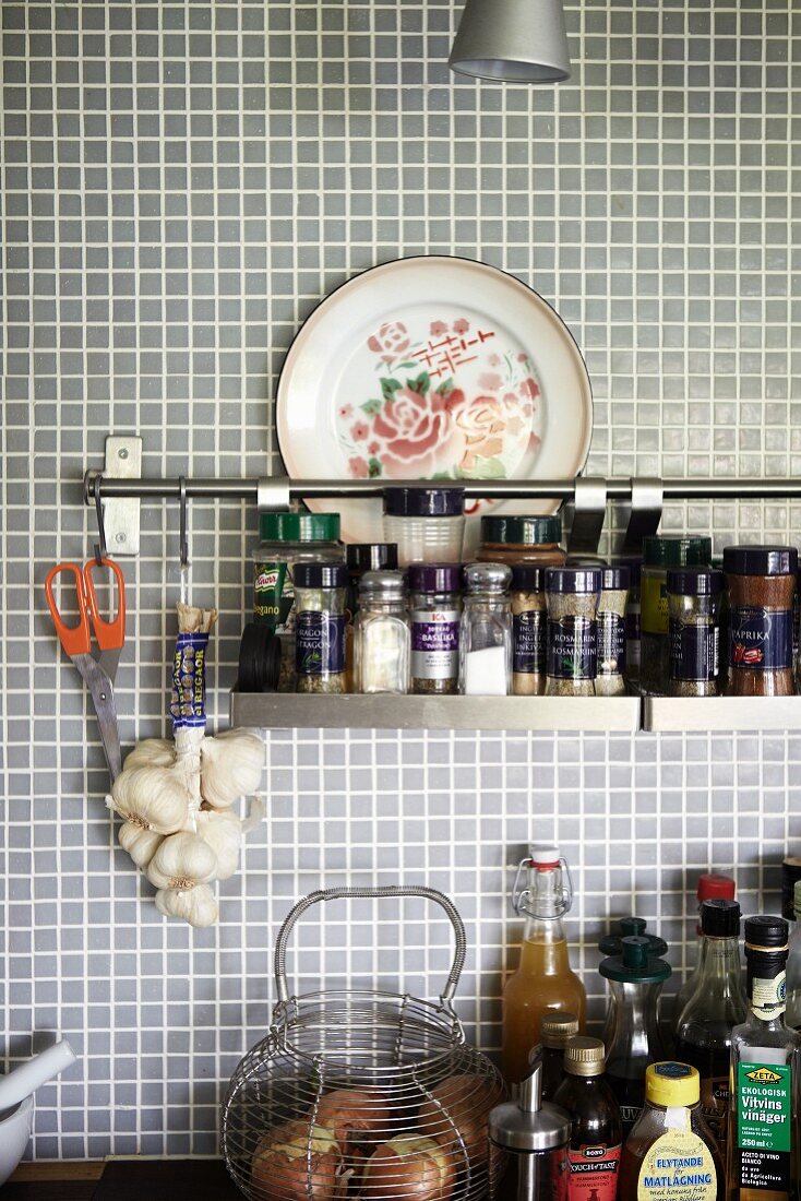 Spice rack hung from rail on pale grey mosaic wall tiles in kitchen