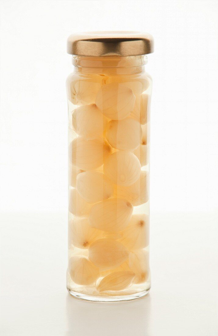 Pickled silver onions in a screw-top jar on a white surface