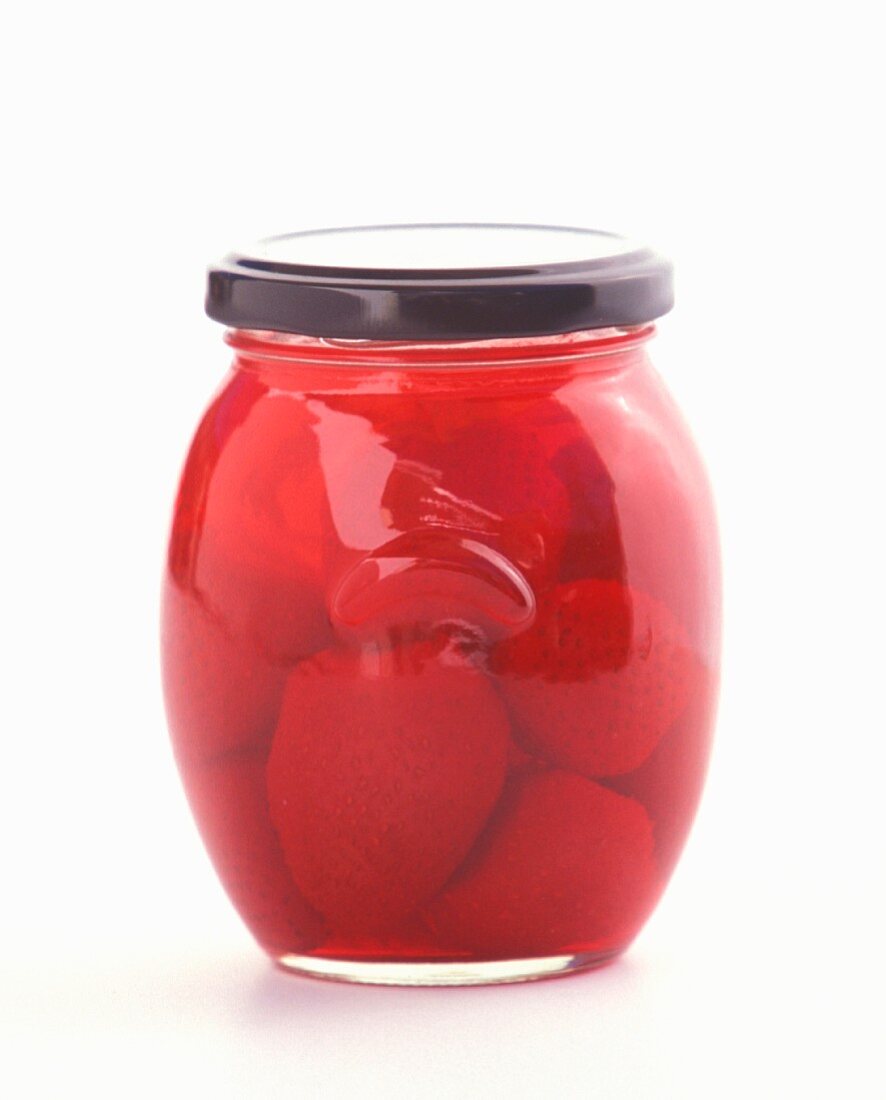 Strawberries preserved in screw-top jar on awhite surface