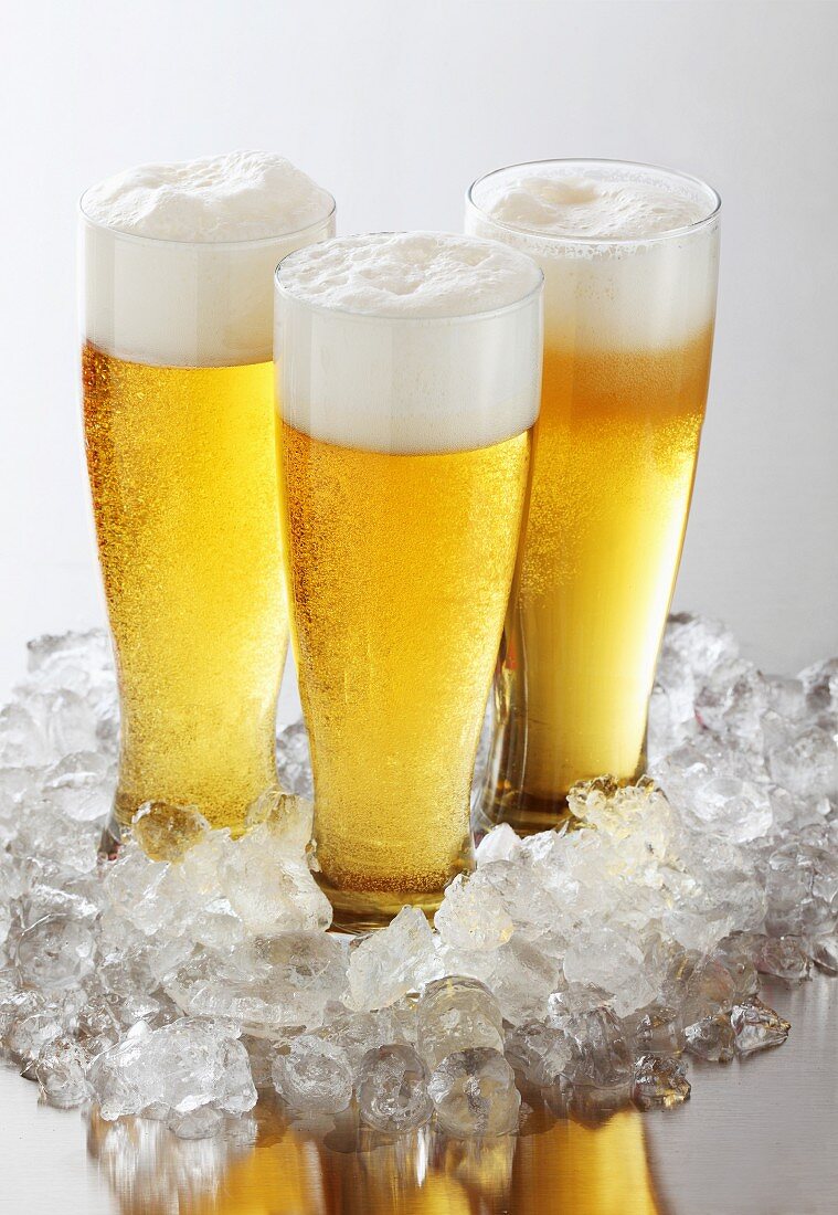 Drei Gläser Bier mit Schaumkronen inmitten von Crushed Ice