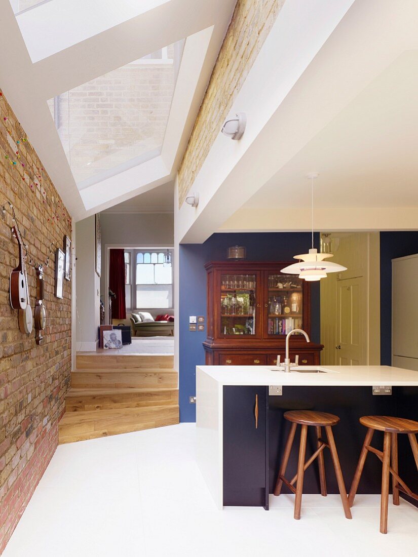 Open-plan kitchen with white tiled floor, modern strip of skylights, brick walls and view into living area