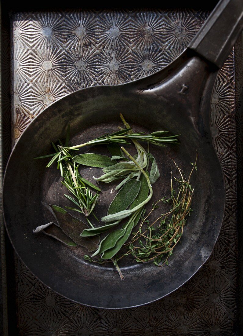Fresh sage, rosemary and thyme in an antique pan (seen from above)