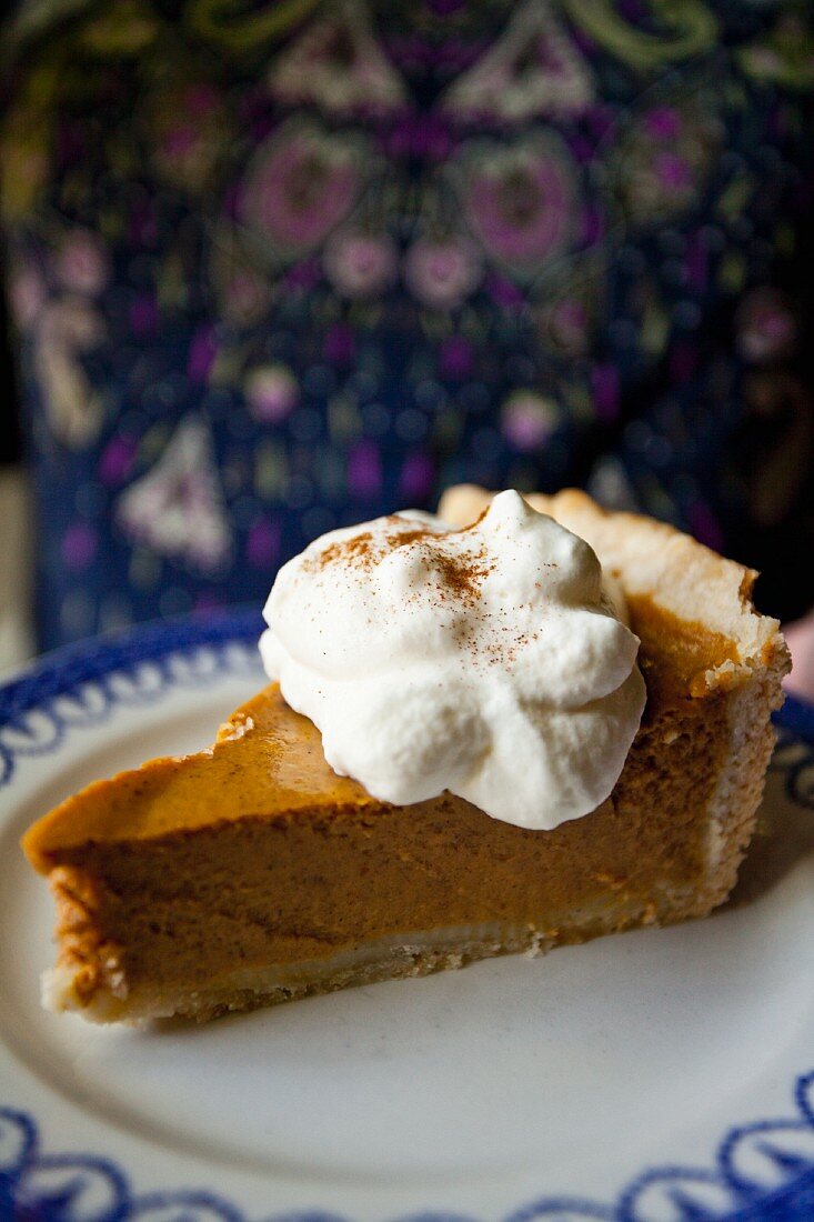 A slice of pumpkin pie with a dollop of cream and blue-and-white plate