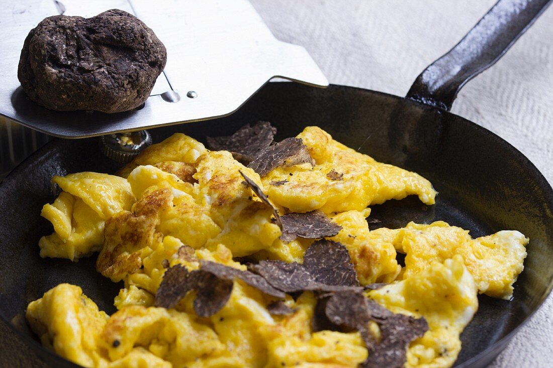 Black Perigord truffles on scrambled eggs in a cast-iron pan with a truffle greater and the whole truffle