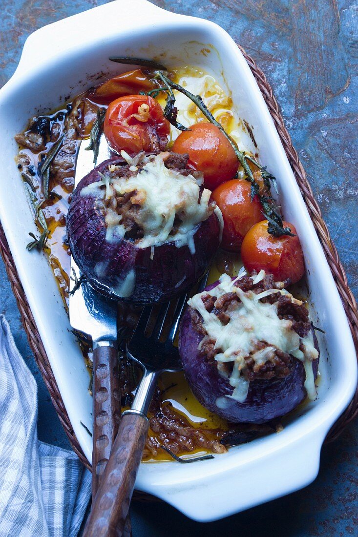 Stuffed red onions gratinated with Parmesan with braised vine tomatoes in a baking dish