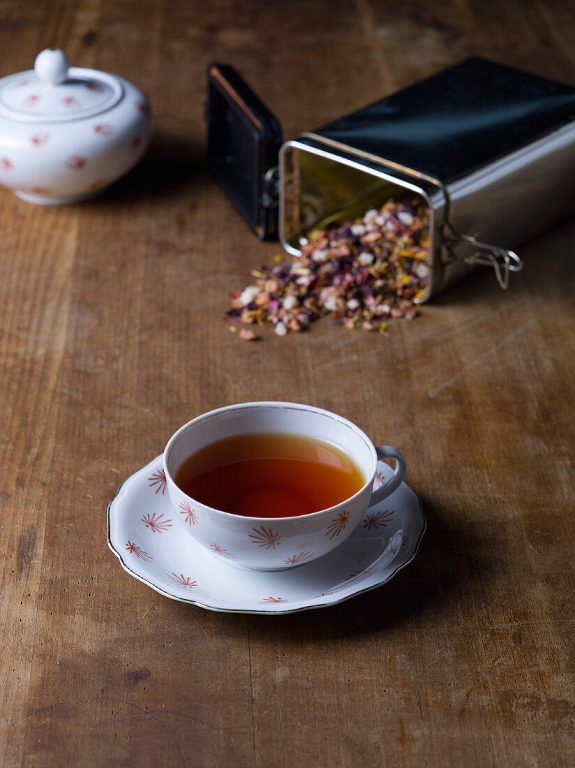 Eine Tasse Kräutertee und Dose mit Teeblättern auf Holztisch