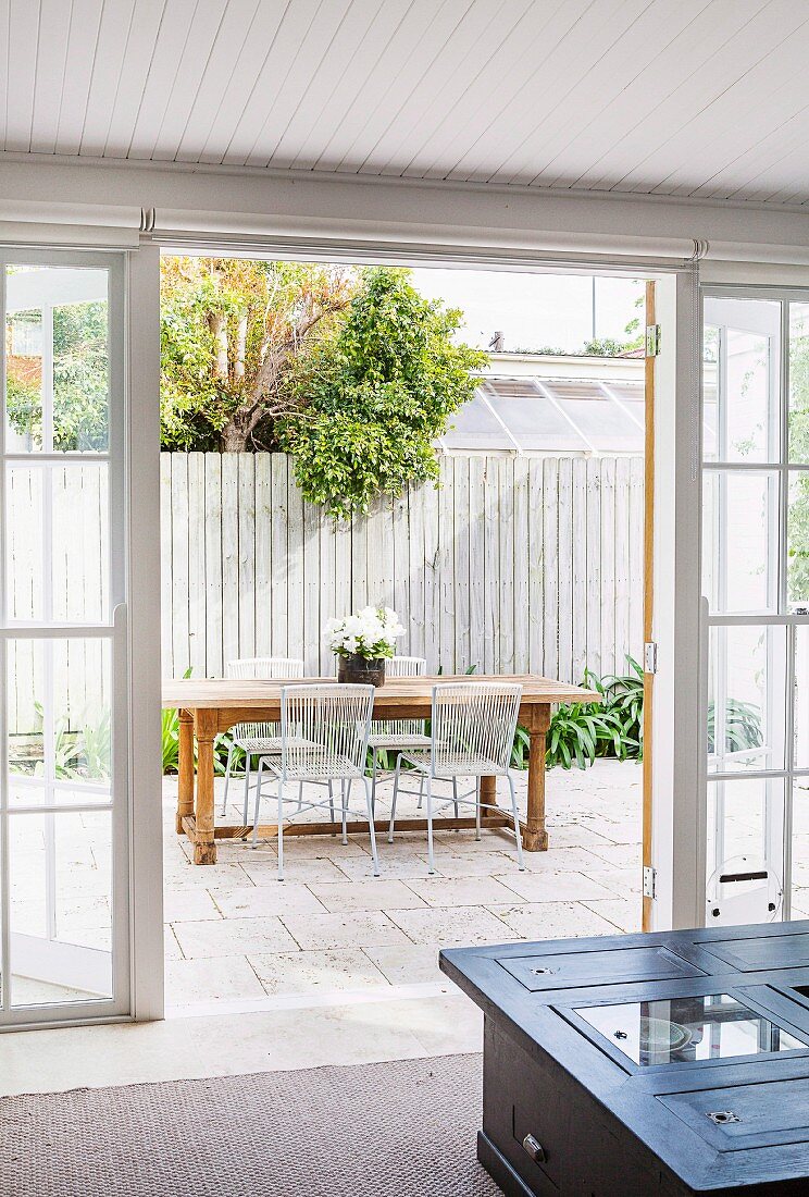 View through open patio door to outdoor dining area in front of white picket fence