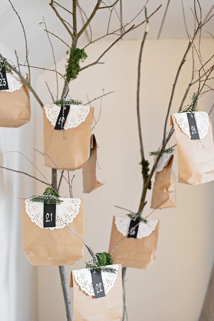 Advent calendar made from paper bags and paper doilies hung from branch