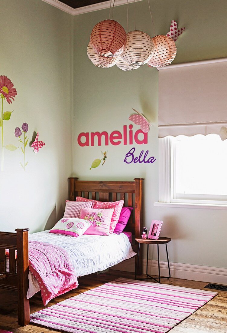 Rosafarbene Kissen auf Holzbett in Mädchenzimmer, an Wand Deko-Buchstaben und Wandtattoos mit Blumenmotiven