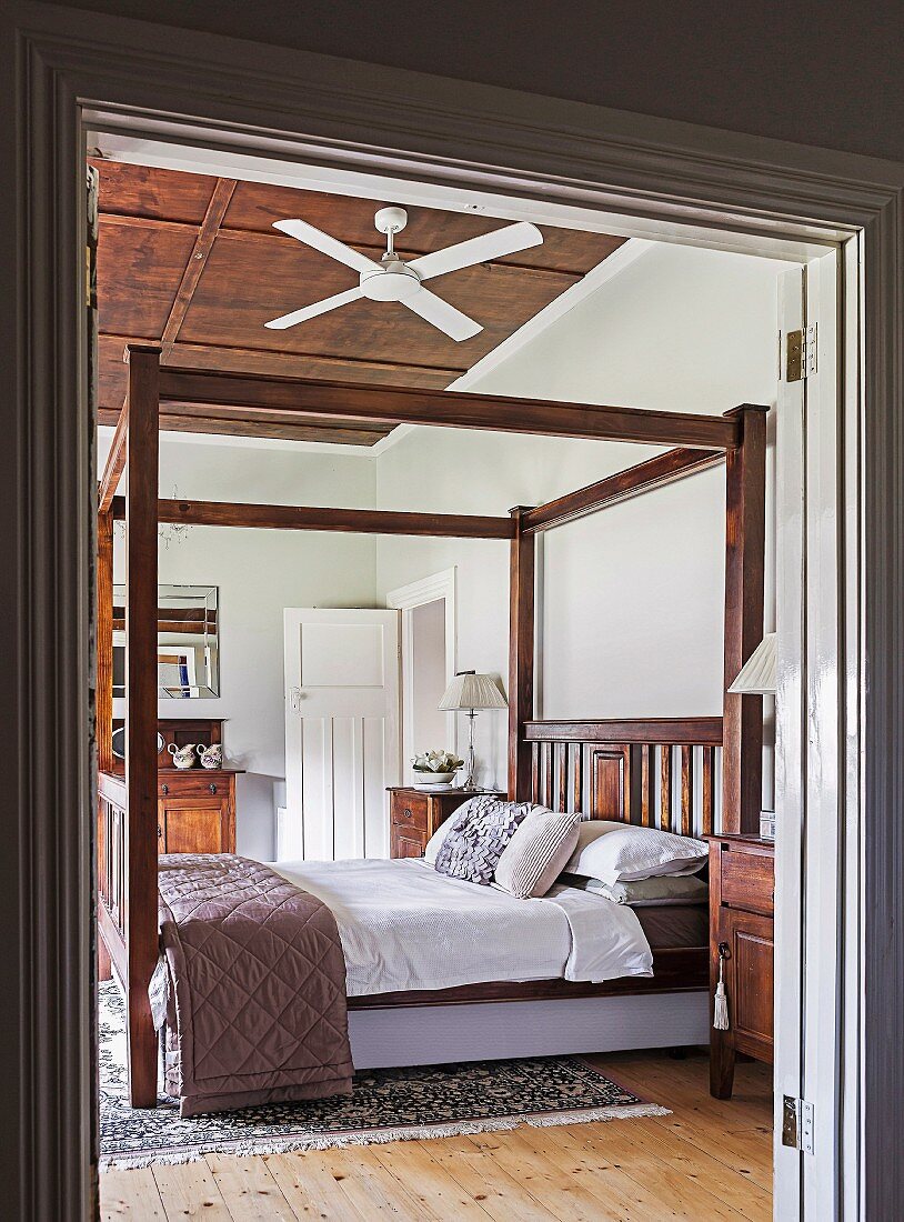 Blick durch offene Flügeltür in Schlafzimmer mit Baldachinbettgestell und Deckenventilator an holzverkleideter Decke