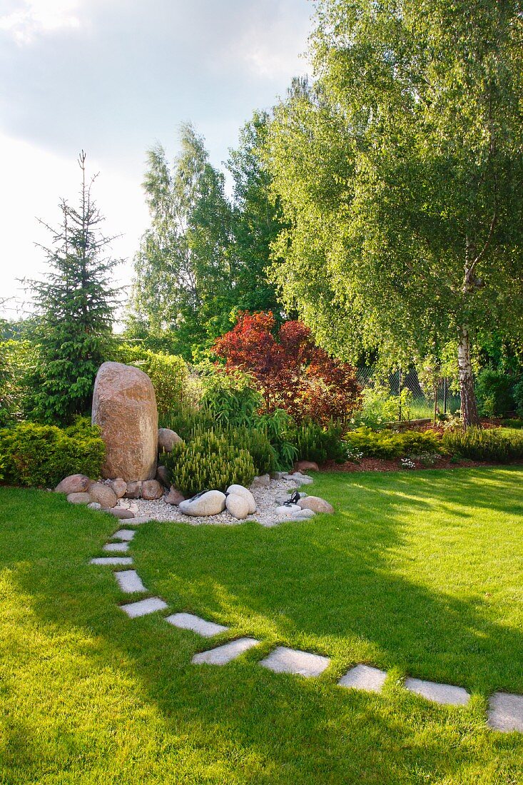 Parkähnlicher Garten mit Findling und Steinplattenweg im Rasen